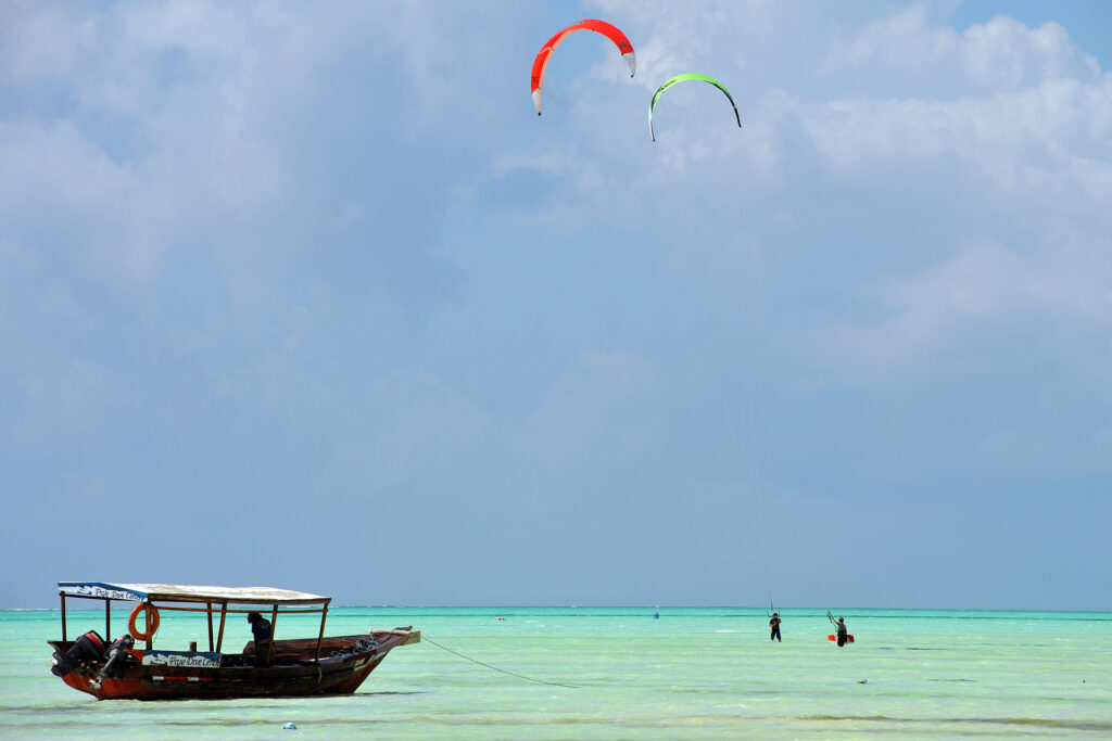 Kitesurfer performing an Air Jibe trick mid-air against a clear blue sky in Zanzibar.
Kitesurfer executing a Back Loop with a fully rotated body over the turquoise waters of Paje Beach, Zanzibar.